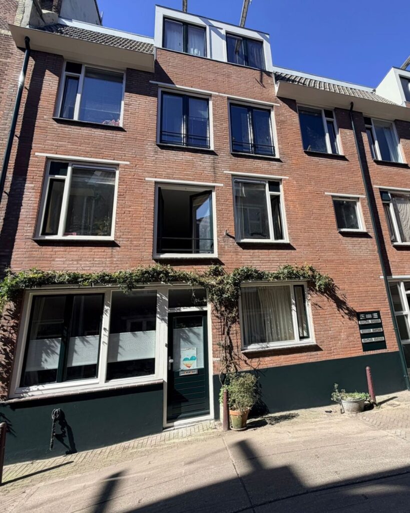 Rode baksteengevel met witte kozijnen en groene plint na buitenschilderwerk in Amsterdam