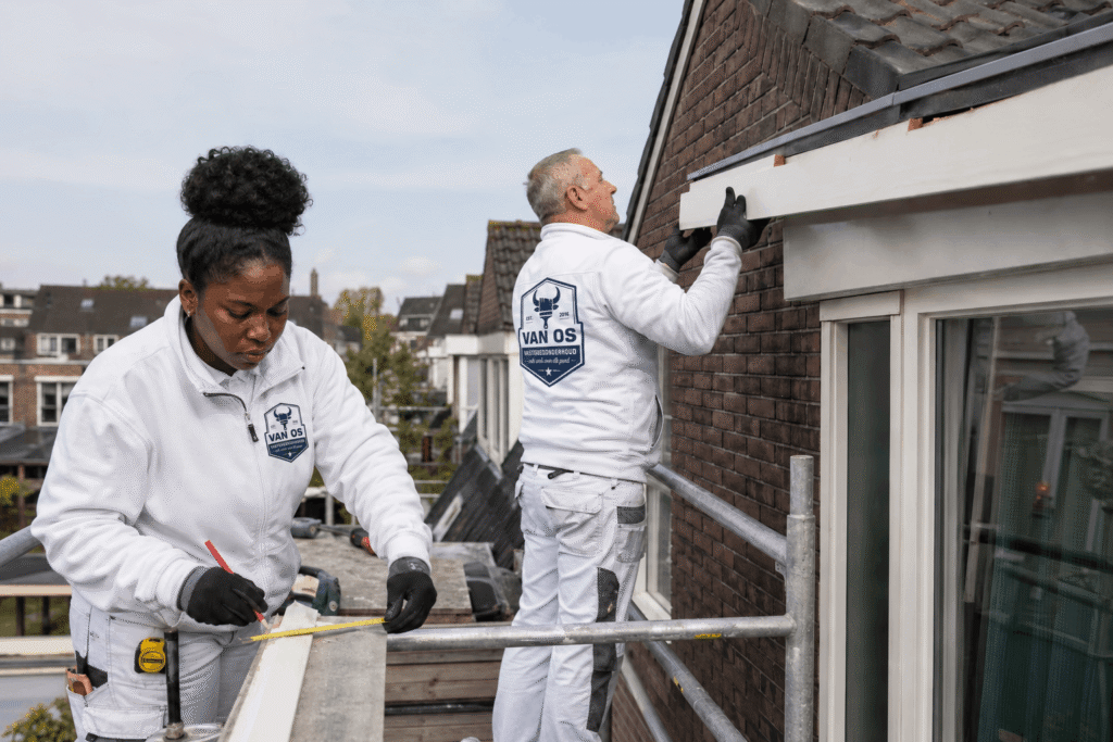 Twee schilders van Van Os op de steiger meten en monteren een houten dakrand tijdens buitenschilderwerk in Amsterdam