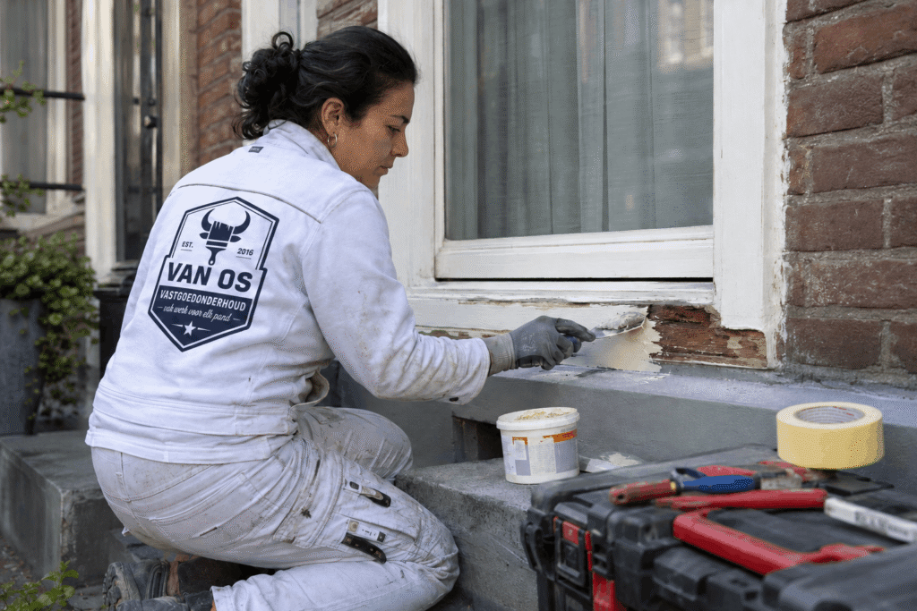Schilder van Van Os brengt plamuur aan op een houten raamdorpel na houtrotherstel in Amsterdam