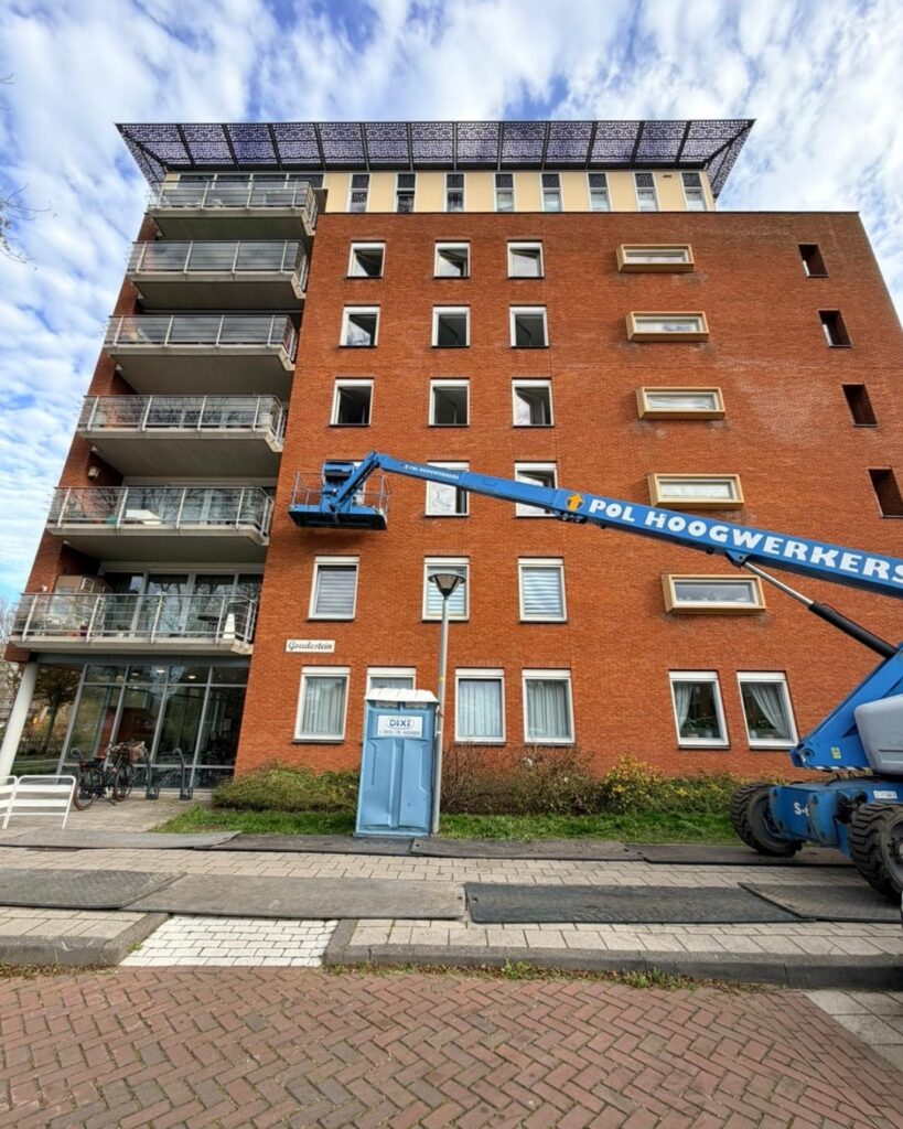Groot bakstenen appartementencomplex met hoogwerker tijdens VvE-onderhoud en buitenschilderwerk in Amsterdam
