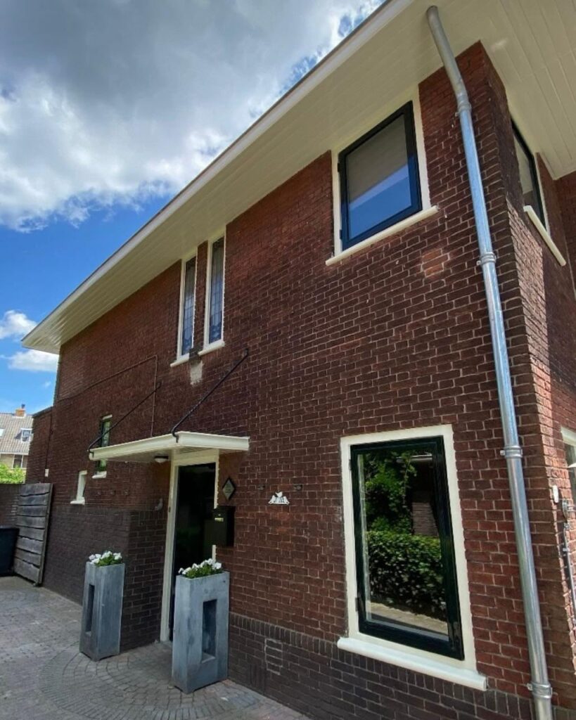 Rode baksteenwoning met creme kozijnen en luifel na buitenschilderwerk
