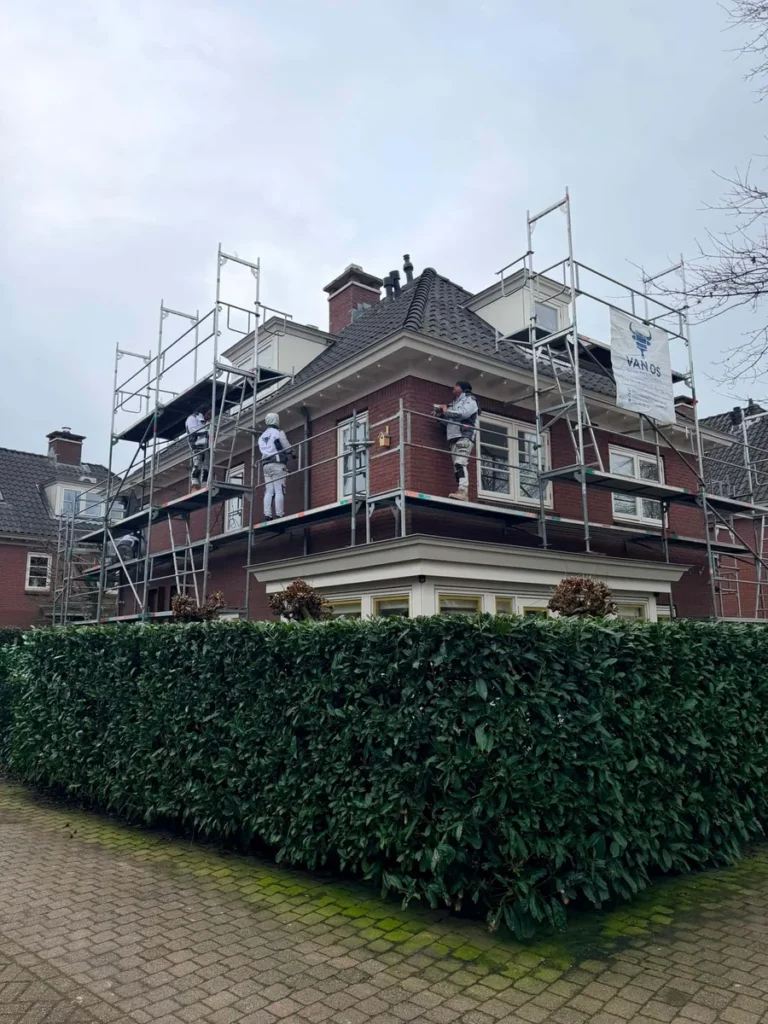 Schilders van Van Os op steiger tijdens buitenschilderwerk aan een bakstenen villa
