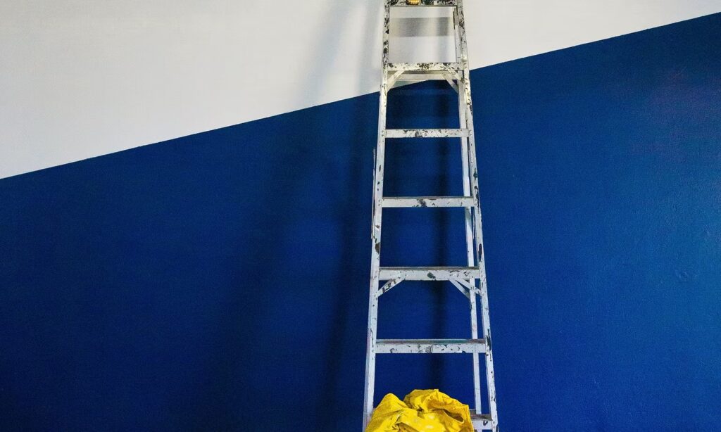 Ladder tegen een half wit, half donkerblauw geschilderde binnenmuur tijdens binnenschilderwerk