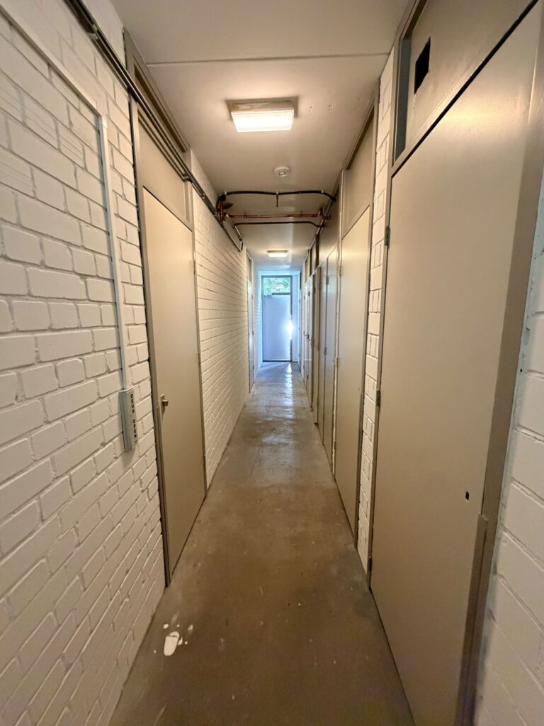 Keldergang met vers gewitte baksteenmuren en creme bergingdeuren na binnenschilderwerk Amsterdam