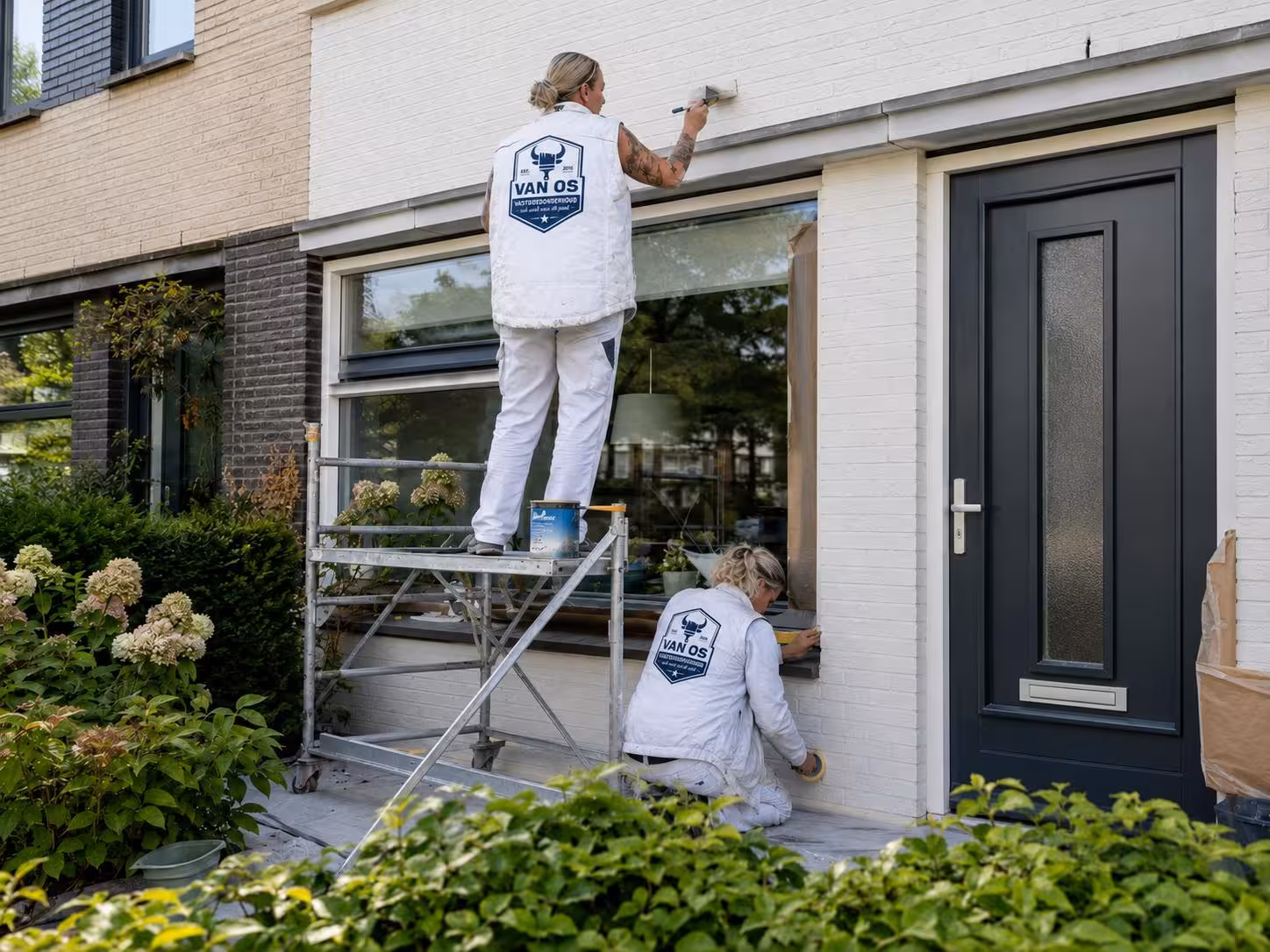 Drie schilders van Van Os aan het buitenschilderwerk van een witte gevel en kozijnen in Amsterdam